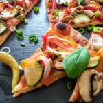 vegane Pizzascheiben belegt mit Zucchini, Zwiebeln, Tomaten, Paprika und frische Basilikumblätter