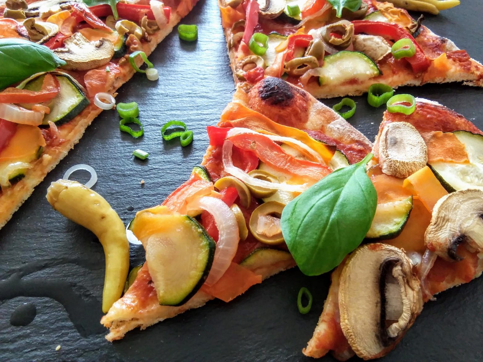 vegane Pizzascheiben belegt mit Zucchini, Zwiebeln, Tomaten, Paprika und frische Basilikumblätter