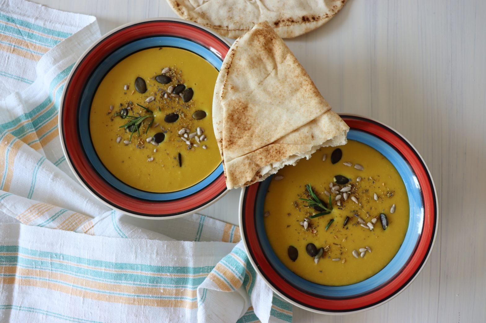 zwei Suppenschalen mit veganer Zitronensuppe dekoriert mit Körner und ein Stück arabisches Fladenbrot