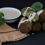 Bunch of backed Falafel balls decorated with fresh cilantro and parsley leafs, tahini sauce and arabic flat bread